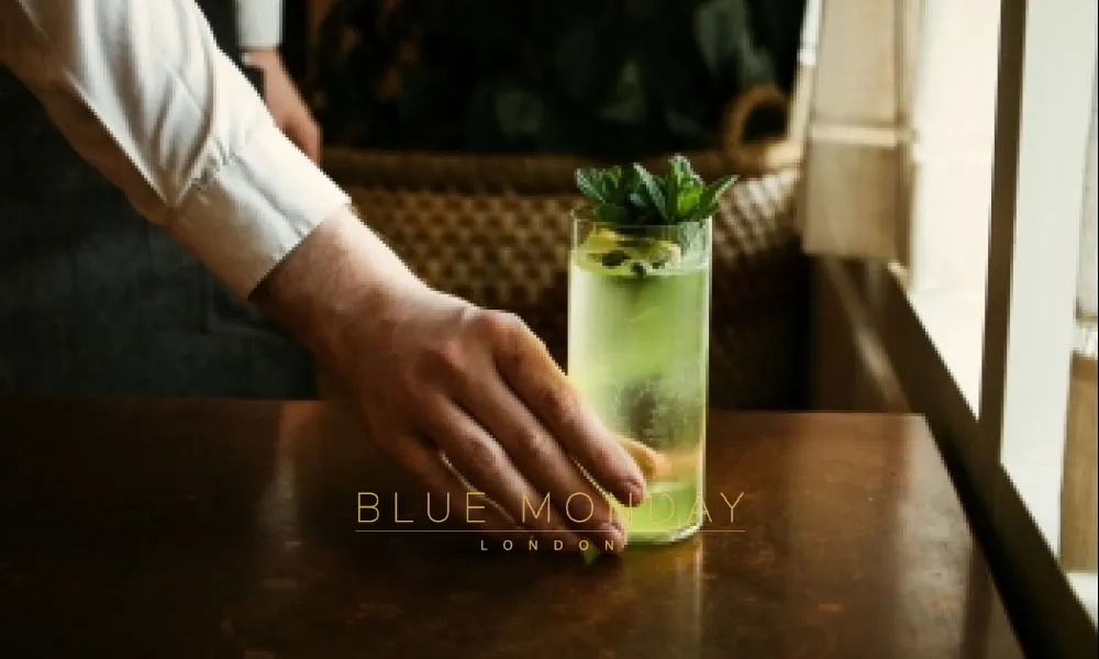 a waiter putting a green cocktail on a table