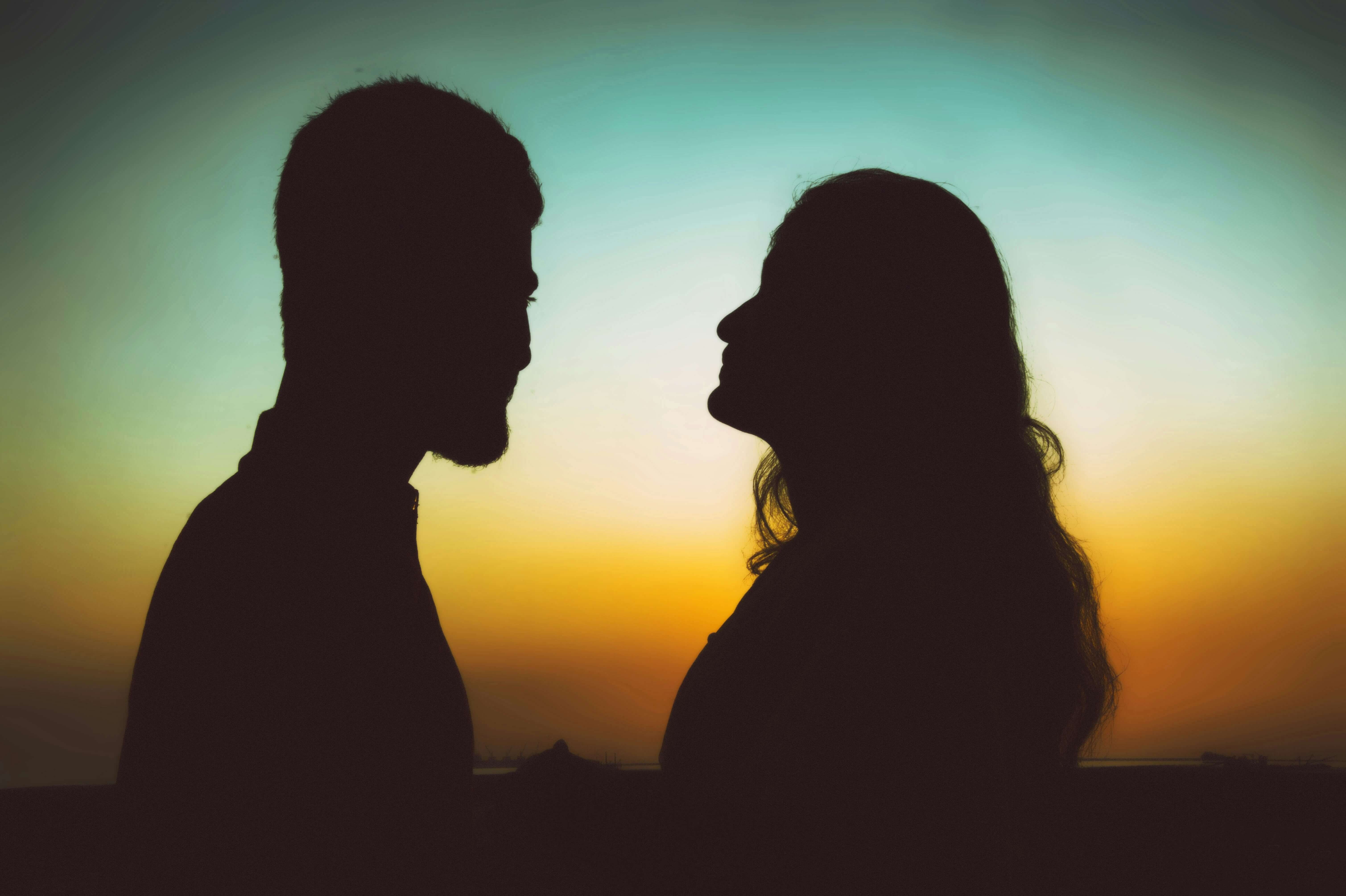 a man and a woman looking at each other with a sunset in the background