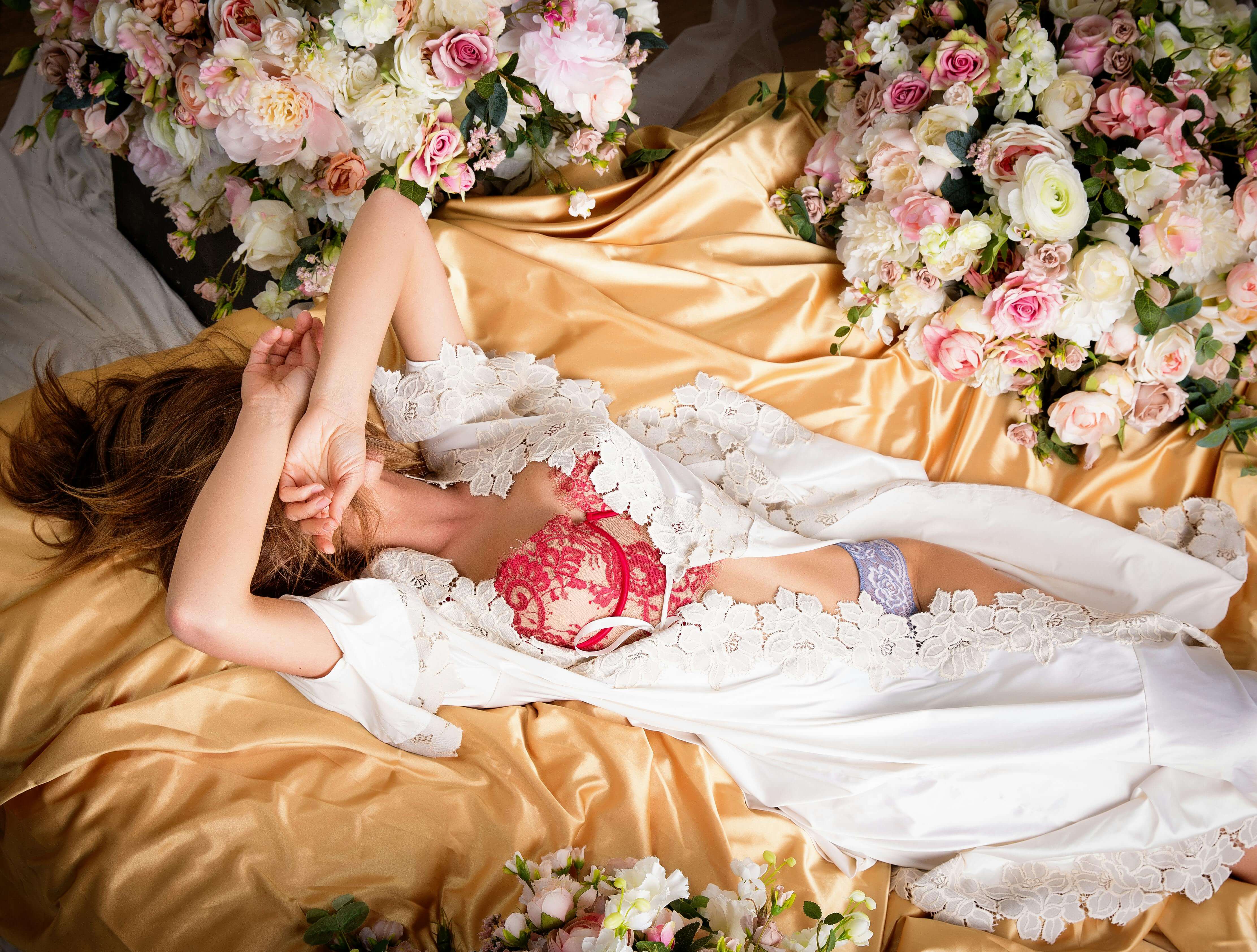 an escort posing on a bed with flowers in lingerie