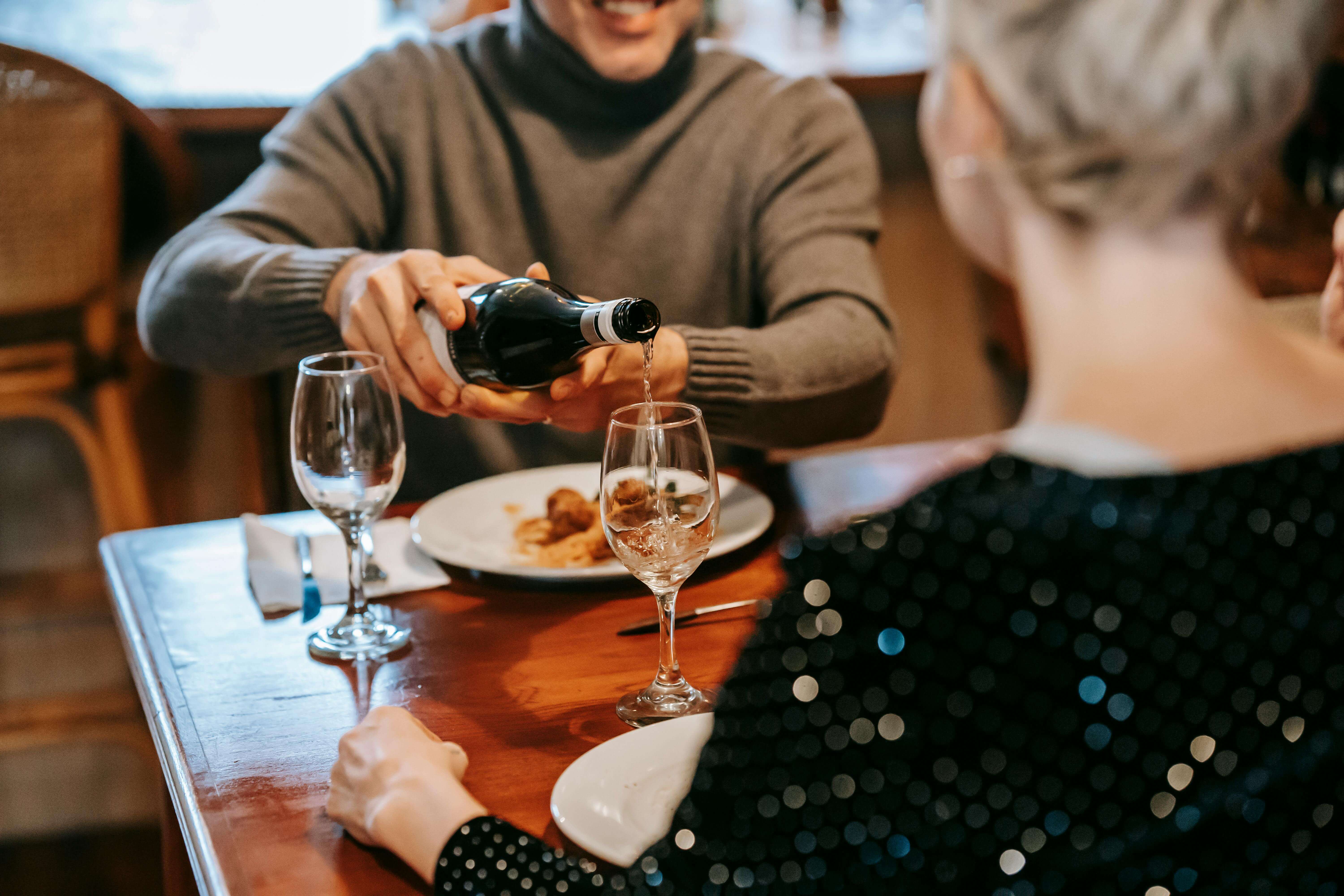 a man pouring wine into a glass on a date with a woman