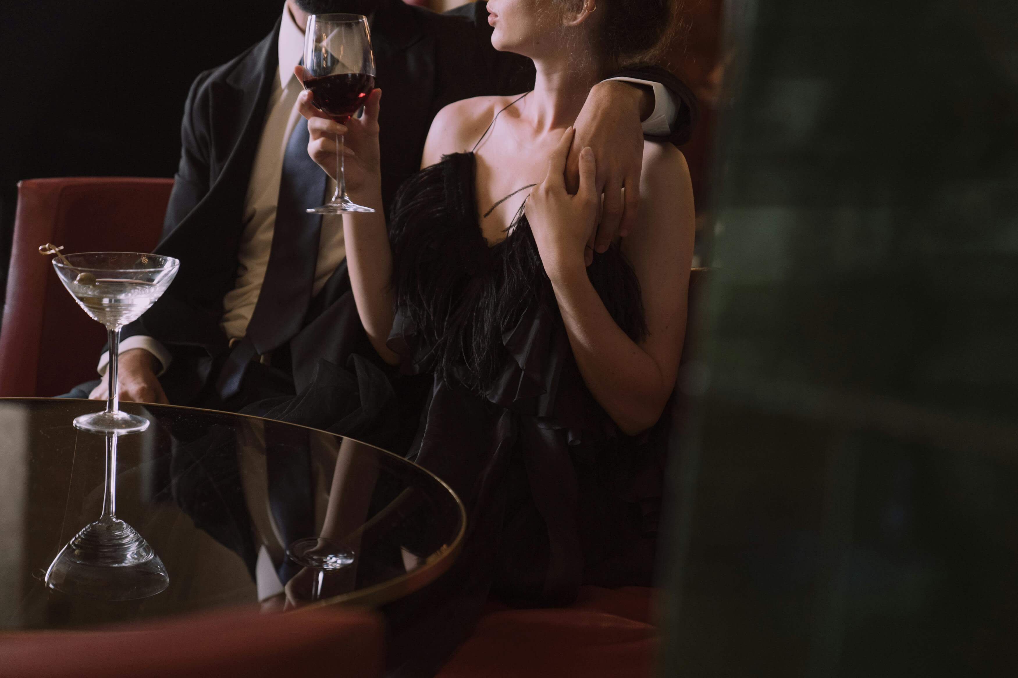 a man in a suit hugging a woman in a dress holding a glass of wine